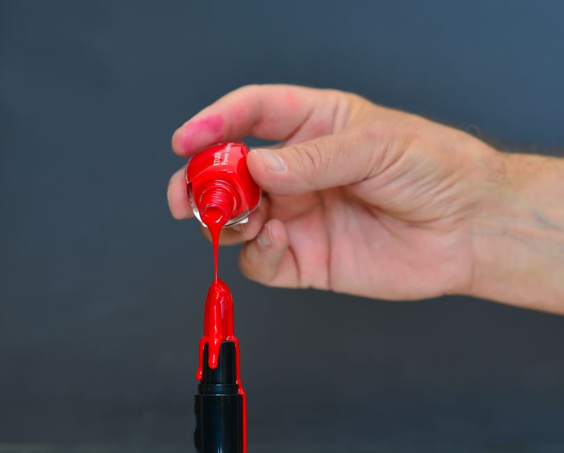 cherry cola lips — Close-up of red nail polish pouring onto lipstick against a dark background, highlighting cosmetic ar