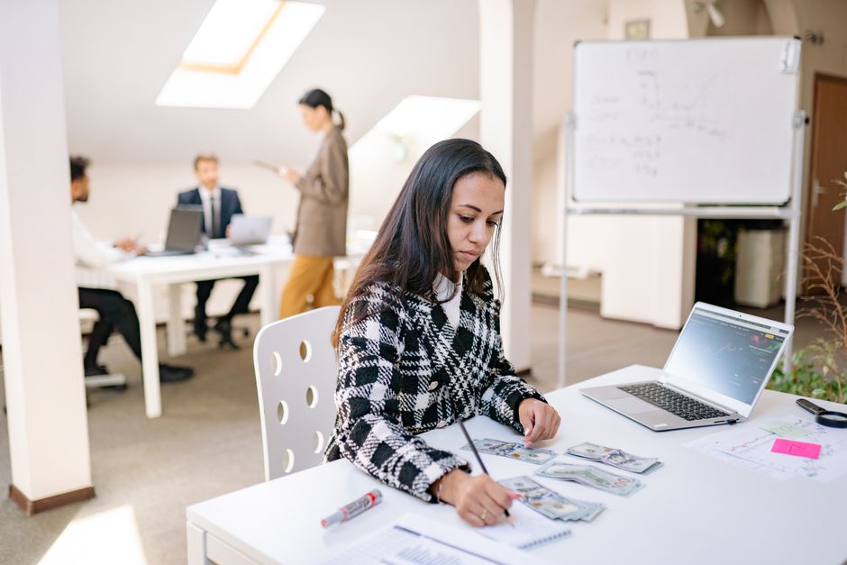 content creator career — Focused businesswoman reviewing financial documents and currency in a modern office setting.