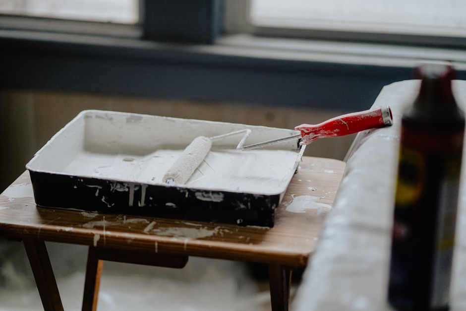 fixxly funding — A paint roller and tray with white paint on a wooden table, indicating a renovation work.
