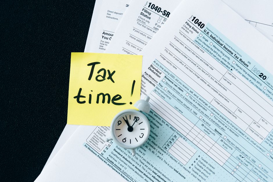 itr filing deadline — A stack of tax forms with a clock and yellow sticky note saying 'Tax time!' indicating urgency.