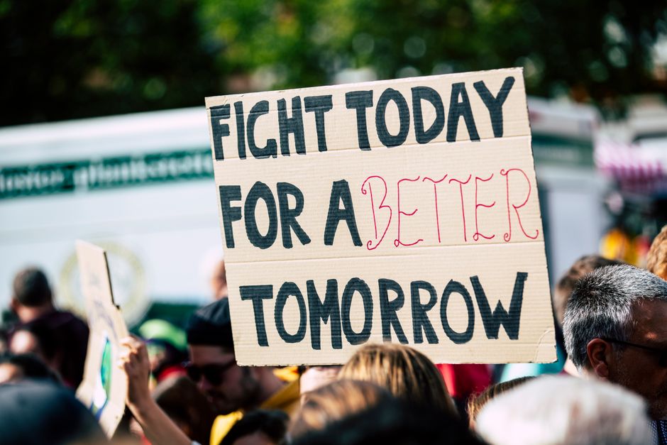 sensex today — Crowd holding a protest sign with 'Fight Today for a Better Tomorrow', outdoors and during the day.