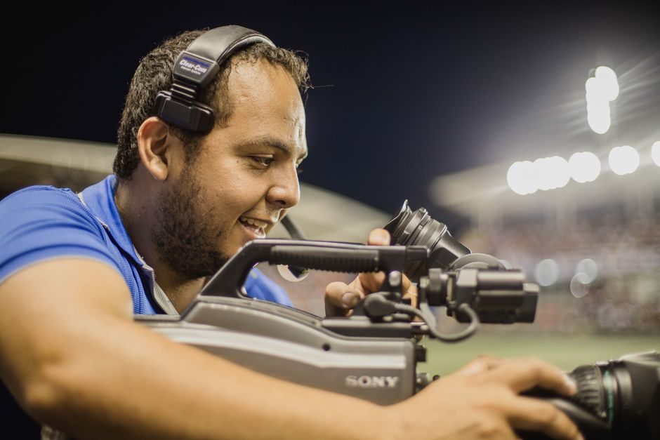vaibhav sooryavanshi record — A cameraman with a headset operates a video camera outdoors at night, focusing on capturin