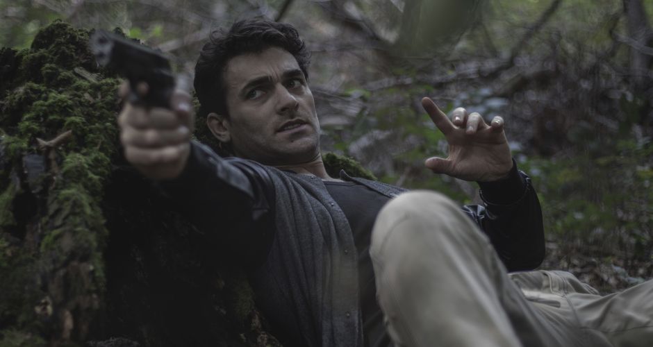 viral food challenge — A man in a forest aims a gun while lying against a mossy tree. Dramatic tension.